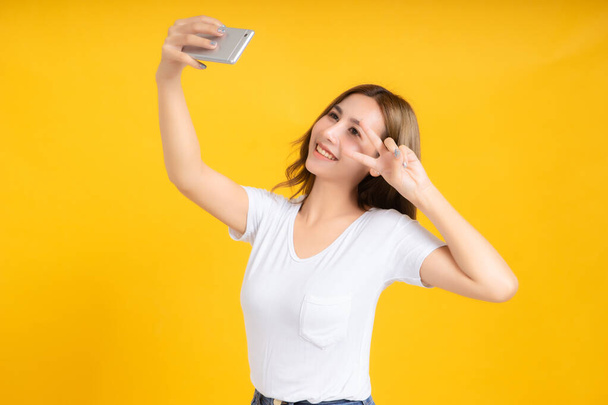 Portrait happy young asian woman laughing finger hands v-sign eye gesture selfie joyful funny positive emotion in white t-shirt, Yellow background isolated studio shot and copy space. - Photo, image
