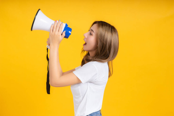 Speaking Loud noise announce of young asian woman with megaphone promotional advertising in white t-shirt smiling emotion on yellow background isolated studio shot with copy space. - Фото, зображення