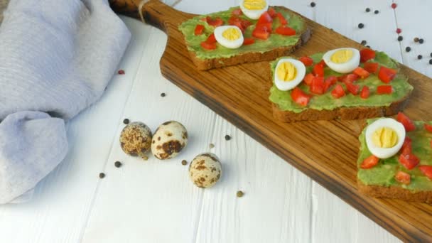 Healthy Vegan food. Spread mashed avocado on a toasted brown bread. Making tasty avocado toast for breakfast. Cooking bruschetta with cherry tomatoes and quail eggs. - Footage, Video