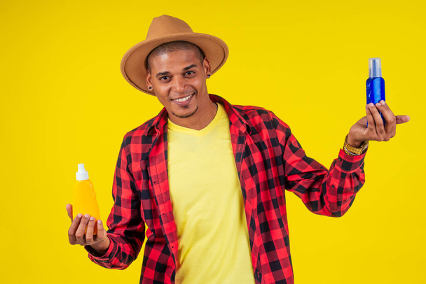 afro brazilian man choosing spf bottle in studio yellow wall - Foto, Imagen