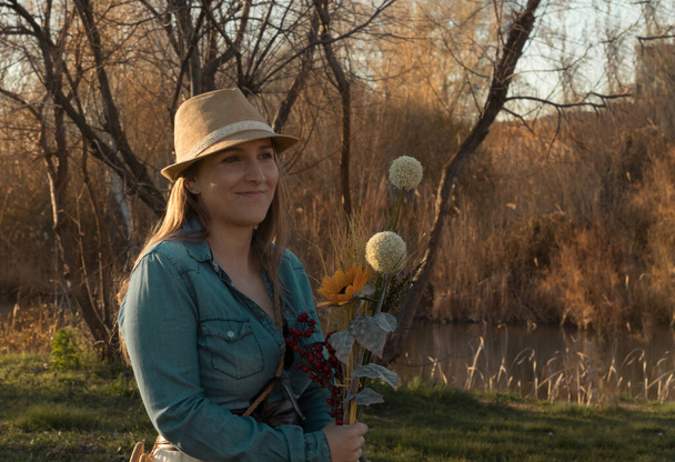 jong blond haar vrouw met boeket van bloemen en cowboy jurk in het veld - Foto, afbeelding