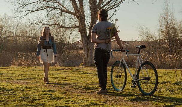 Sötét hajú férfi vár egy nőre a biciklijével és egy csokor virággal. - Fotó, kép