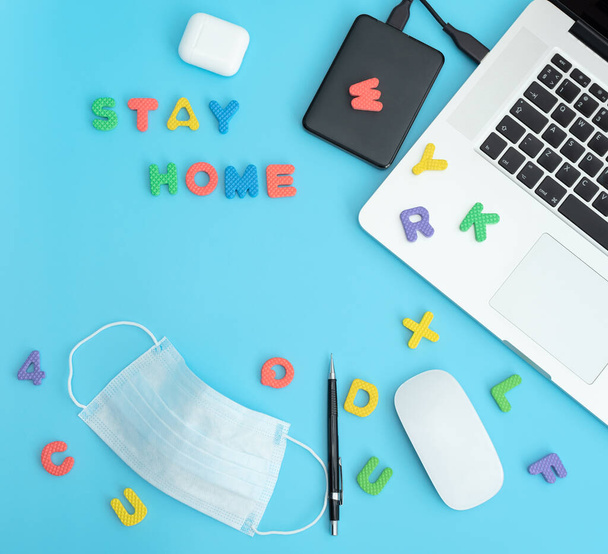 Stay home concept. Mockup, top view of workplace with laptop, earphones, mouse, pencil, letters and protective medical face mask. Remote work and education during coronavirus pandemic in the world. - Foto, Imagem