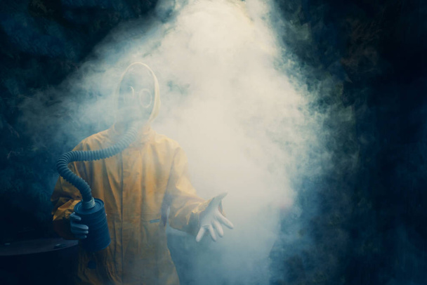Kobieta w masce gazowej z elastyczną gumową rurką do oddychania w żółtej ochronnej całości w dymie. Od koronawirusu i ochrony przed gazem. Zanieczyszczenie środowiska - Zdjęcie, obraz