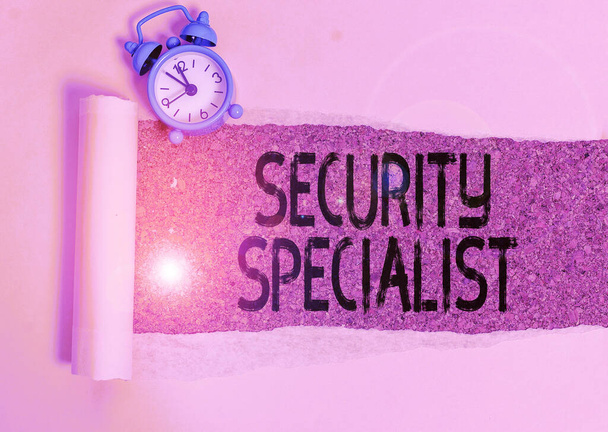 Writing note showing Security Specialist. Business photo showcasing specializes in the security of showing assets or systems Alarm clock and torn cardboard on a wooden classic table backdrop. - Photo, Image