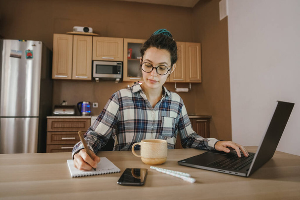 Egy nő jegyzeteket tart egy noteszben egy távoli munkában otthon. Otthoni munka. - Fotó, kép