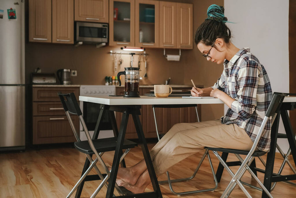 Женщина работает дома на кухне за обеденным столом. В расслабленном положении. Карантин
. - Фото, изображение