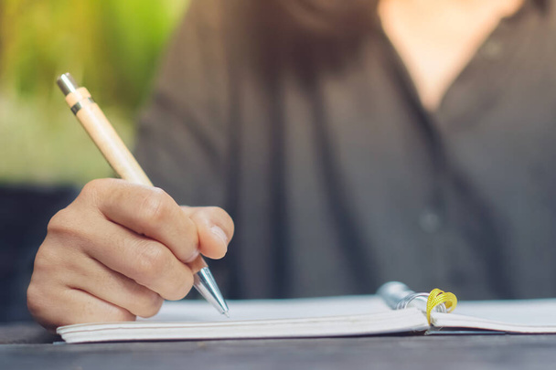 Femme écriture à la main dans un petit carnet de notes blanc pour prendre une note à ne pas oublier ou à faire un plan de liste pour l'avenir. - Photo, image