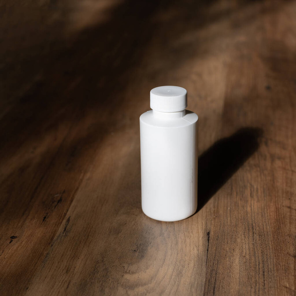 木製の背景と影に白いボトル。キャップ付き化学溶剤ボトル - 写真・画像
