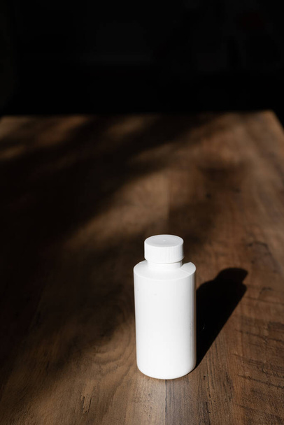 Biała butelka na drewnianym tle i cieniu. Butelka z rozpuszczalnikiem chemicznym z zakrętką - Zdjęcie, obraz