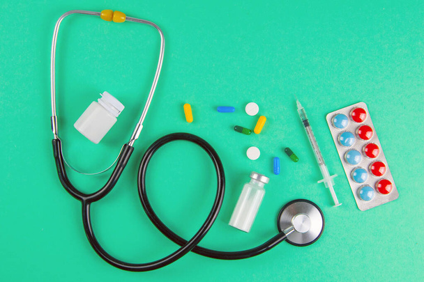 Studio shot of stetoscope, syringe and pills on light green background. Top views. - Foto, imagen