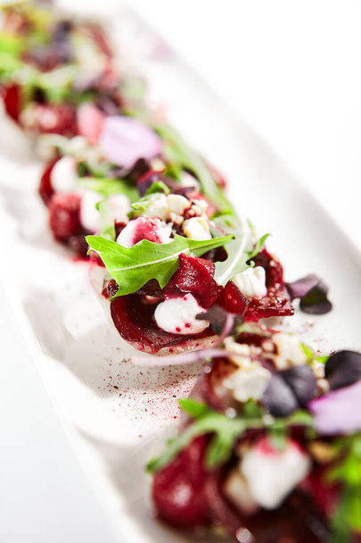 Beetroot tartare with goat cheese on tray. Delicious snacks with arugula and spices. Haute cuisine. Restaurant vegetable apperizers served with fresh greenery. Food presentation, culinary recipe - Φωτογραφία, εικόνα