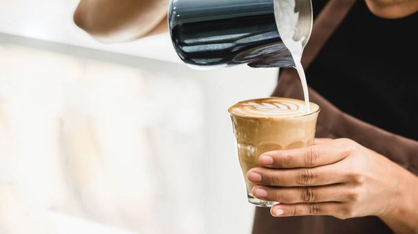 Professionelle Barista gießt gedämpfte Milch in Kaffeeglastasse und macht schöne Latte Art Rosetta Muster im Café - Foto, Bild