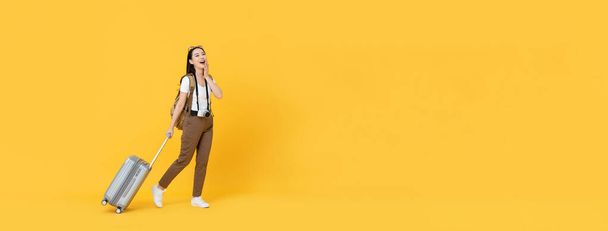 Happy young Asian tourist woman with baggage going to travel on holidays isolated on yellow banner background with copy space - Foto, afbeelding