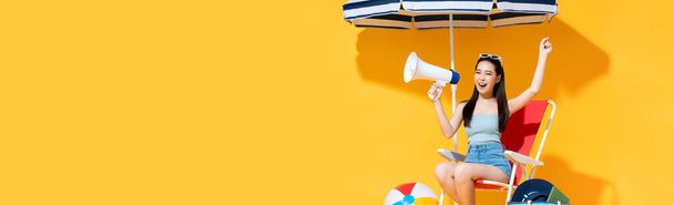 Ecstatic beautiful young Asian woman announcing on megaphone in sunny yellow isolated banner background with copy space - Photo, Image