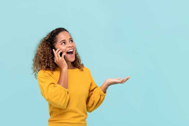 Талия до портрета молодой веселой афроамериканской женщины счастливо взявшись за телефон делая открытый жест ладони в изолированном светло-голубом фоне студии
 - Фото, изображение