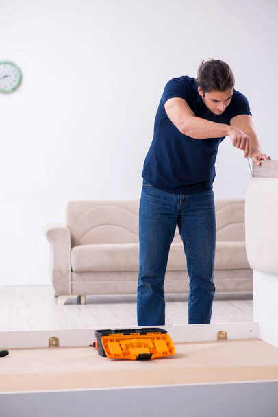 Junger männlicher Bauunternehmer installiert Möbel zu Hause - Foto, Bild