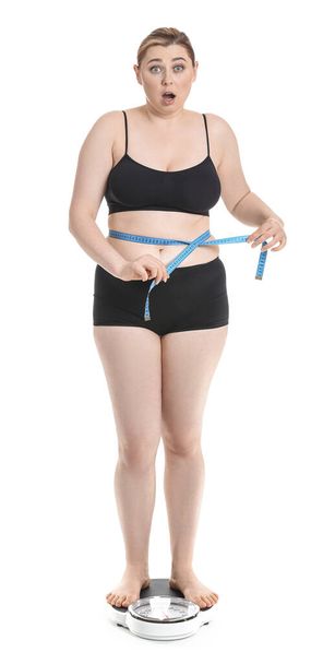 Shocked overweight woman standing on scales against white background. Weight loss concept - Foto, immagini