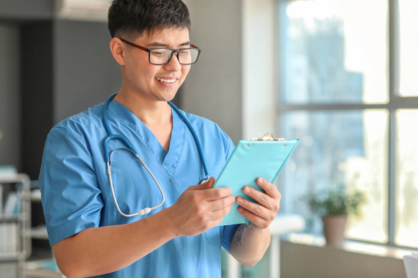 Male Asian doctor with clipboard in clinic - Zdjęcie, obraz