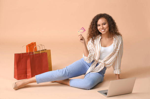 Jeune femme avec ordinateur portable, carte de crédit et sacs à provisions sur fond de couleur
 - Photo, image