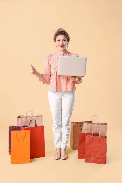Beautiful young woman with laptop and shopping bags on color background - Photo, Image