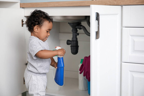 Pequeño bebé afroamericano jugando con detergentes en casa. Niño en peligro
 - Foto, imagen
