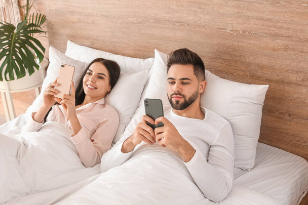 Jeune couple avec des téléphones portables couchés dans le lit à la maison
 - Photo, image