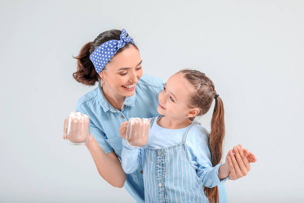 Woman and her little daughter with tasty cocoa drink on light background - Photo, Image