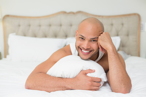 Smiling casual bald young man lying in bed - 写真・画像