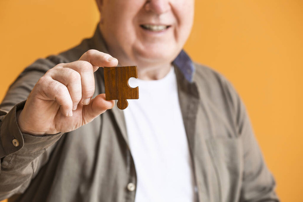Elderly man suffering from mental disability with puzzle piece on color background, closeup - Фото, изображение