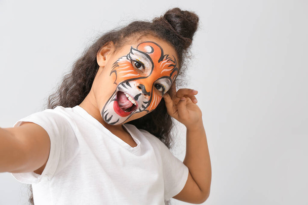 Vicces afro-amerikai lány arcfestés szelfi a fény háttér - Fotó, kép