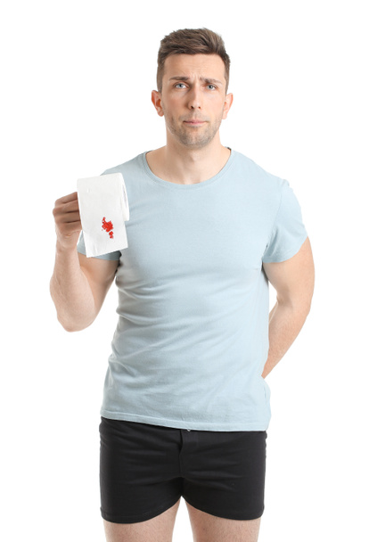 Jeune homme tenant du papier toilette avec tache de sang sur fond blanc. Concept des hémorroïdes
 - Photo, image