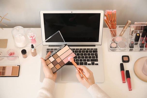 Make-up kunstenaar aan tafel met moderne laptop en cosmetica - Foto, afbeelding