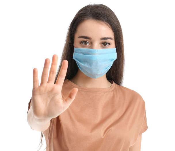 Jonge vrouw met medisch masker toont STOP gebaar tegen witte achtergrond - Foto, afbeelding