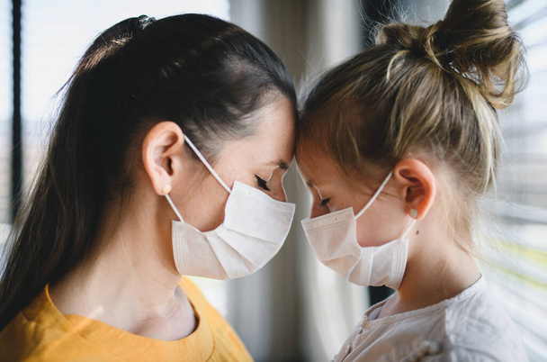 Mother and child with face masks indoors at home, Corona virus and quarantine concept. - Fotografie, Obrázek