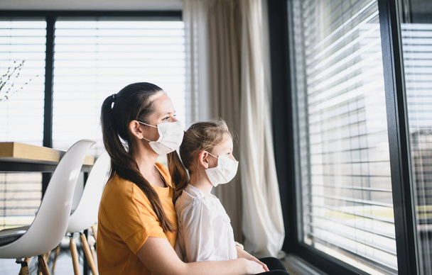 Mother and child with face masks indoors at home, Corona virus and quarantine concept. - Foto, Imagem