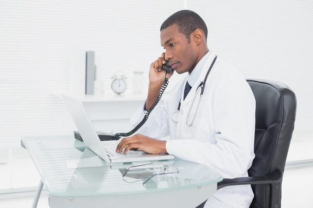 Male doctor using phone and laptop at medical office - Foto, Bild