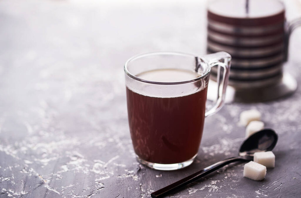 Café con natillas en una taza de vidrio, cuchara, terrones de azúcar, natillas sobre un fondo de hormigón. Bebida de café
 - Foto, imagen