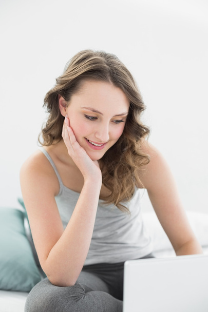 Smiling casual brunette looking at laptop in bed - Φωτογραφία, εικόνα