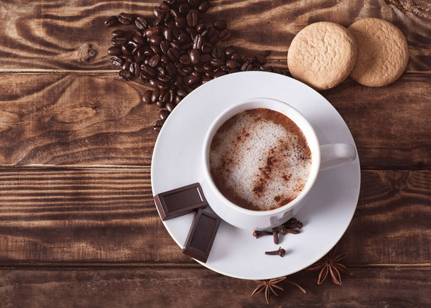 filiżanka kawy z pianką, czekoladą, ciastkami, ziarenkiem kawy w kształcie serca na drewnianym stole. Flat Lay bez ludzi - Zdjęcie, obraz