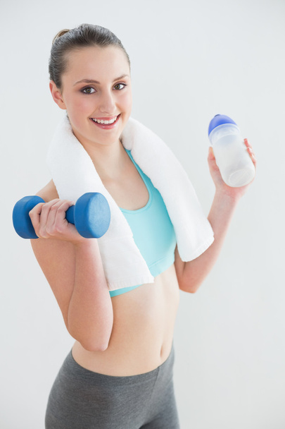 Woman with dumbbells and water bottle against wall - 写真・画像