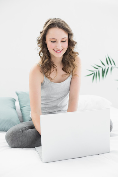 Smiling casual brunette looking at laptop in bed - Fotoğraf, Görsel