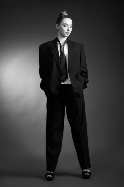 Beautiful sexy young blonde woman in a dark business suit, white shirt and tie posing on a gray background - Φωτογραφία, εικόνα