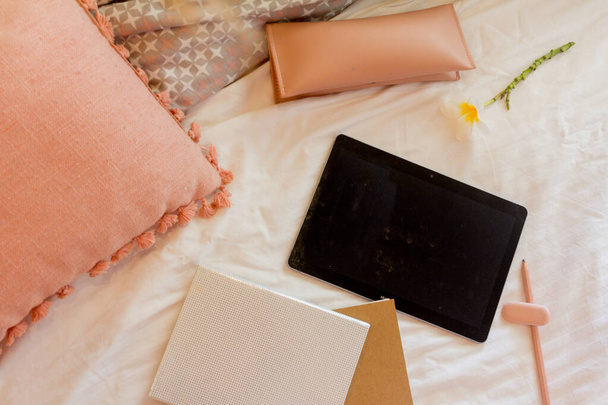 Comprimido vazio, dois cadernos, estojo de lápis e almofada rosa na cama
 - Foto, Imagem