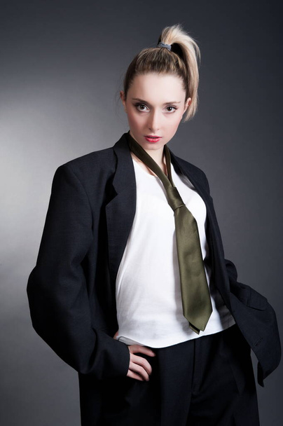 Beautiful sexy young blonde woman in a dark business suit, white shirt and tie posing on a gray background - Zdjęcie, obraz