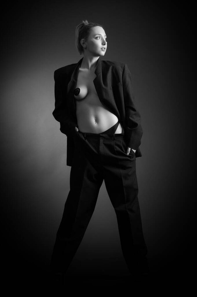 Beautiful sexy young blonde woman in a dark business suit on a naked body posing on a gray background - Foto, afbeelding