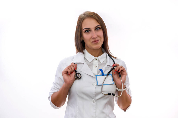 Mulher sorridente em casaco médico branco posando com estetoscópio isolado em branco
 - Foto, Imagem