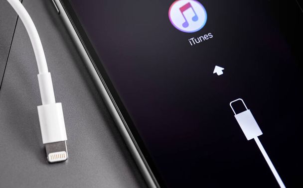 Смартфон Apple iPhone с кабелем Lightning, логотипом iTunes на экране. Apple - это многонациональная технологическая компания, которая занимается проектированием, разработкой, онлайн-сервисами. Москва, Россия - 12 июля 2019 года - Фото, изображение
