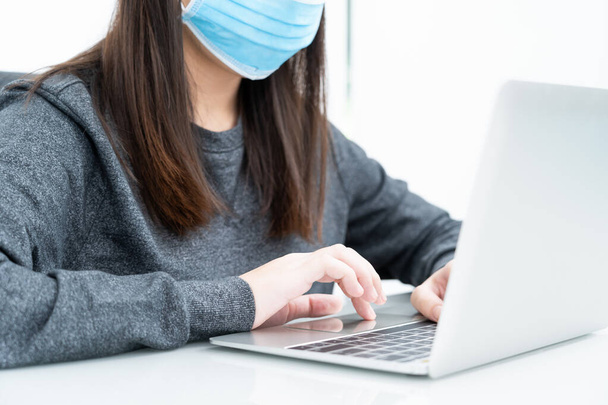 Woman using a laptop computer on the desk at home and wearing protective mask for protection against virus Covid-19 - Fotografie, Obrázek