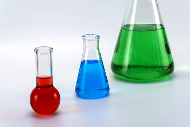 Laboratory glassware with liquid on white background. glass chemical flask with reagent. glass technical vessel used in chemical laboratories. Erlenmeyer flask is used in a trimetric analysis. - Foto, afbeelding